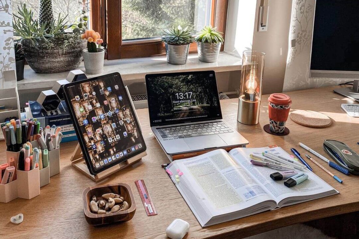 Bureau d'étudiant avec un manuel ouvert, des surligneurs, une tablette et un ordinateur portable